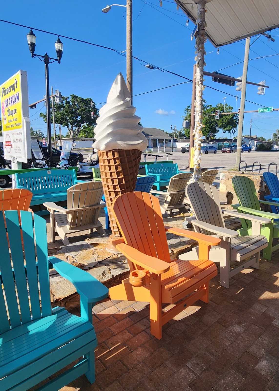 Colorful Adirondack chairs and a giant soft-serve cone statue on the patio at Pinecraft Ice Cream Shoppe