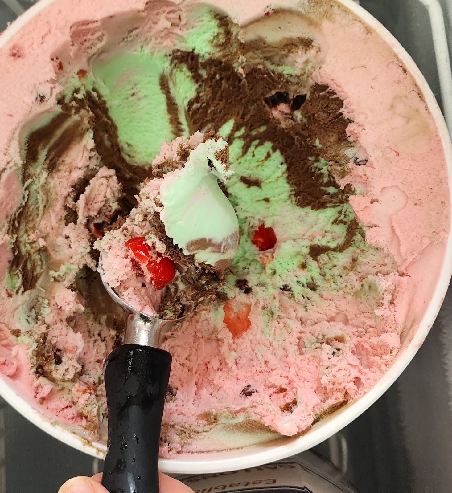 An open tub of marbled pink, mint and chocolate homemade ice cream being scooped at Pinecraft